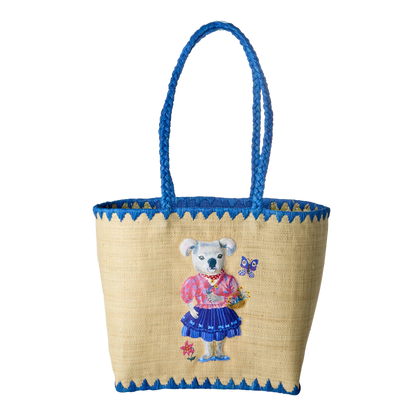 Taske i raffia materiale med blå kant og hank. På midten er motivet af en koala bjørn med tøj på omkringet af sommerfugle og blomster.