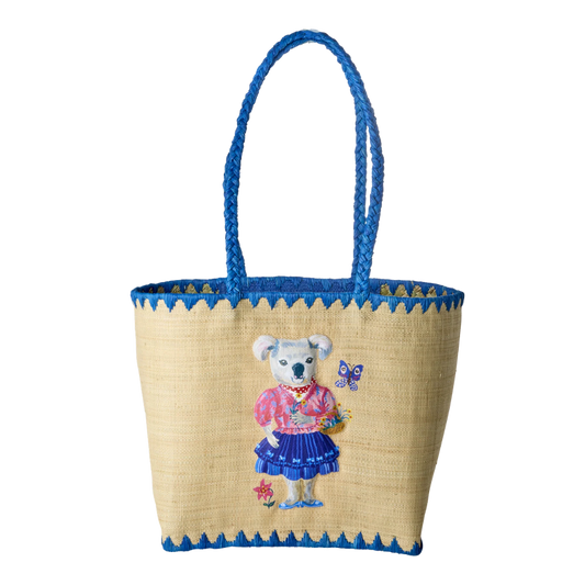 Taske i raffia materiale med blå kant og hank. På midten er motivet af en koala bjørn med tøj på omkringet af sommerfugle og blomster.