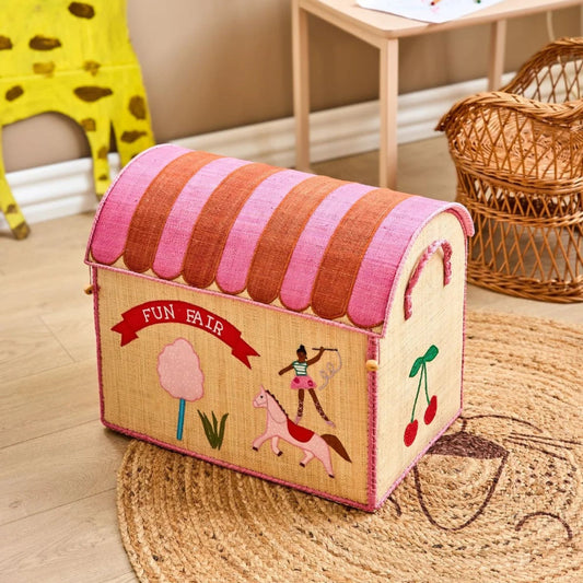 Kurv til opbevaring formet som et hus. Huset er brunt med et låg som er stripet af pink og rød. Den er dekoreret med candy floss, en linedanser, kirsebær og andre sjove Fun fair motiver.